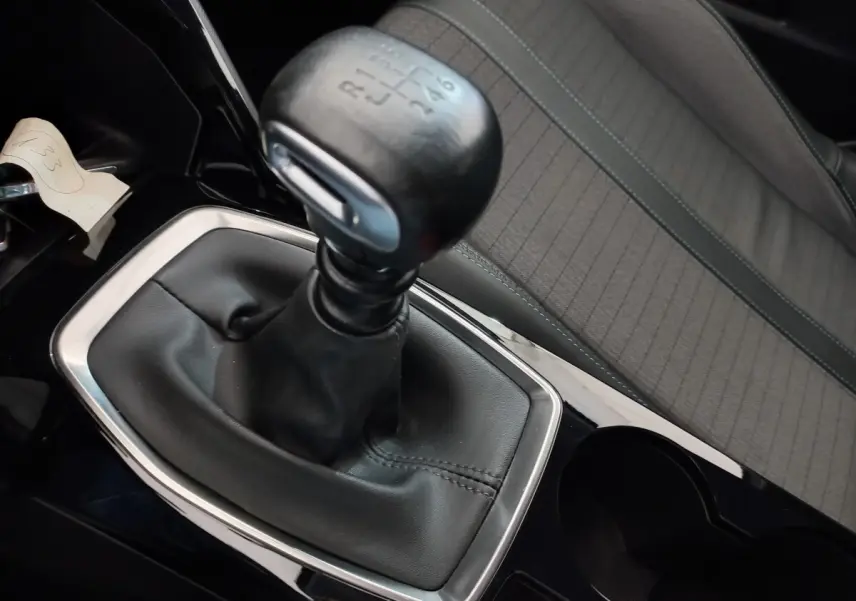 Gros plan sur le levier de vitesse manuel noir et la sellerie grise du siège avant droit d'une Peugeot 208 blanche.