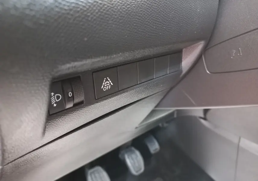 Gros plan sur les commandes de réglage des phares et désactivation de l'alerte de franchissement de ligne côté conducteur d'une Peugeot 208 blanche.