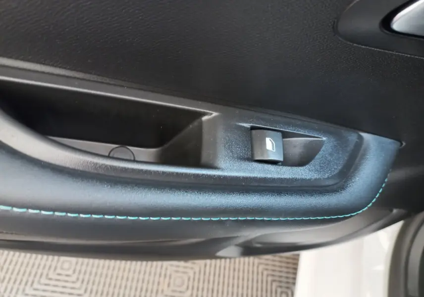 Détail de la commande de lève-vitre sur la porte côté conducteur d'une Peugeot 208 blanche avec surpiqûres bleues.