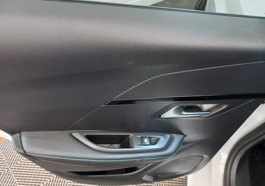 Gros plan sur la porte intérieure côté gauche d'une Peugeot 208 blanche, avec poignée argentée et surpiqûres bleues.
