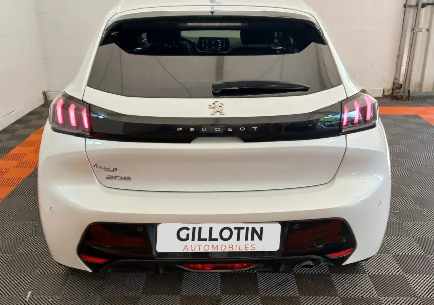 Vue arrière d'une Peugeot 208 blanche avec feux LED allumés et logo Peugeot visible sur le hayon.