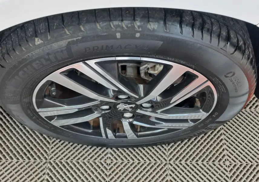 Gros plan sur la jante alliage noire et argentée avec logo Peugeot, pneu Michelin Primacy 4 sur Peugeot 208 blanc.