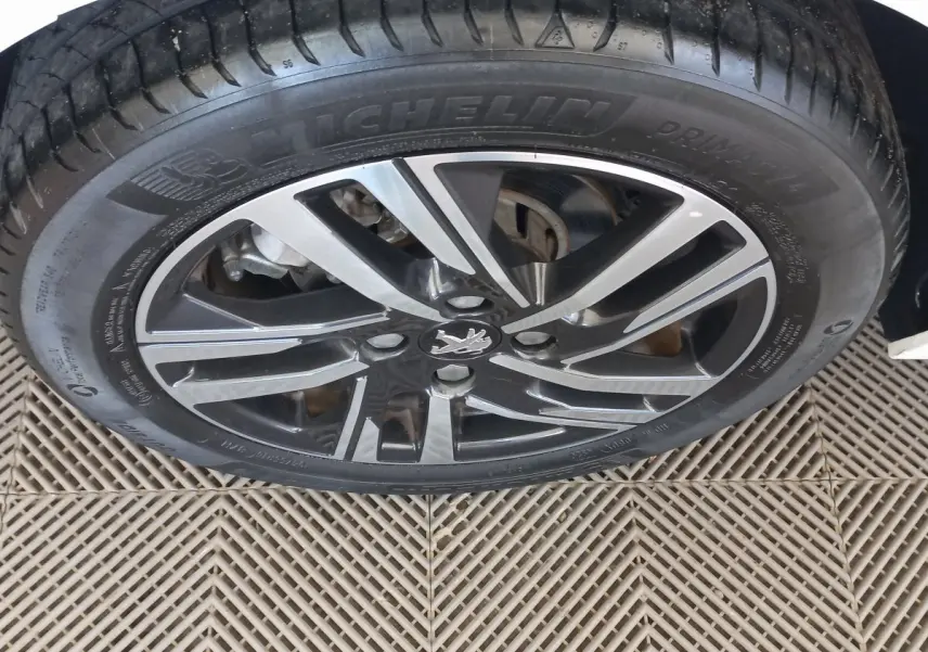 Gros plan sur la roue avant gauche blanche d'une Peugeot 208 PureTech 100 S&S Allure avec jante alliage noire et argentée.