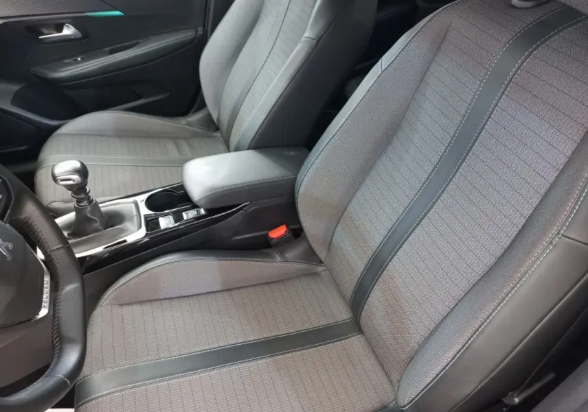 Vue intérieure côté conducteur de la Peugeot 208 PureTech 100 S&S Allure 2021, sièges tissu gris avec surpiqûres noires.