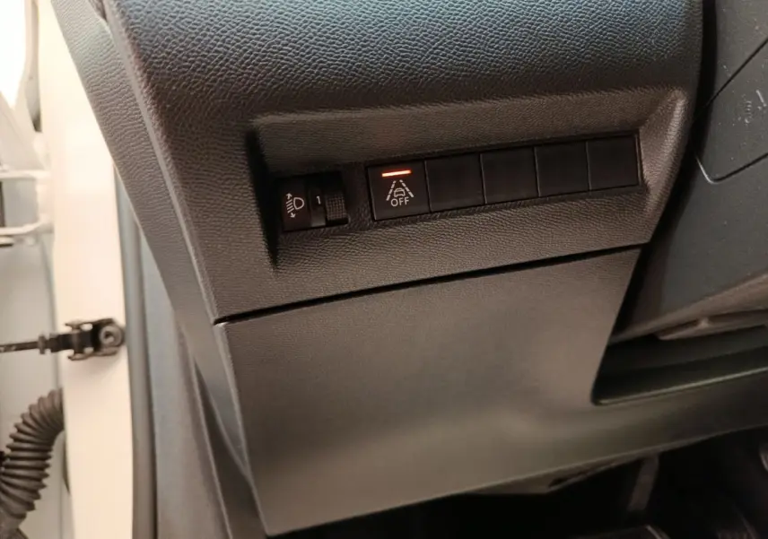 Détail intérieur côté gauche du tableau de bord noir avec commandes d’éclairage et d’aide à la conduite activée.