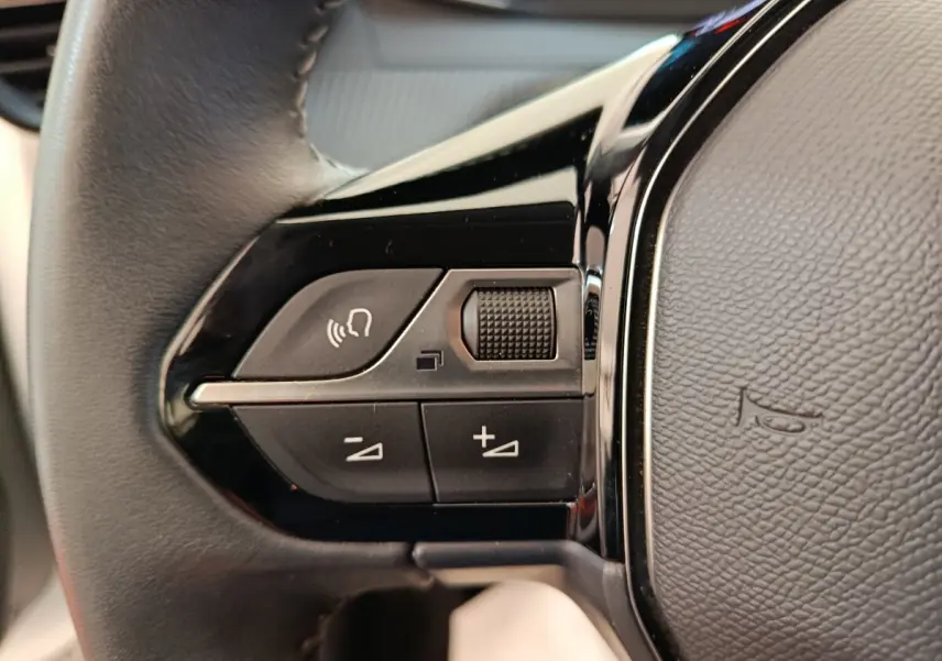 Gros plan sur les commandes gauche du volant cuir noir du Peugeot 208 électrique blanc, avec boutons multifonctions.