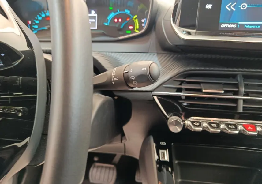Vue intérieure rapprochée du tableau de bord et volant de la Peugeot 208 électrique, avec commandes et écran tactile visibles.