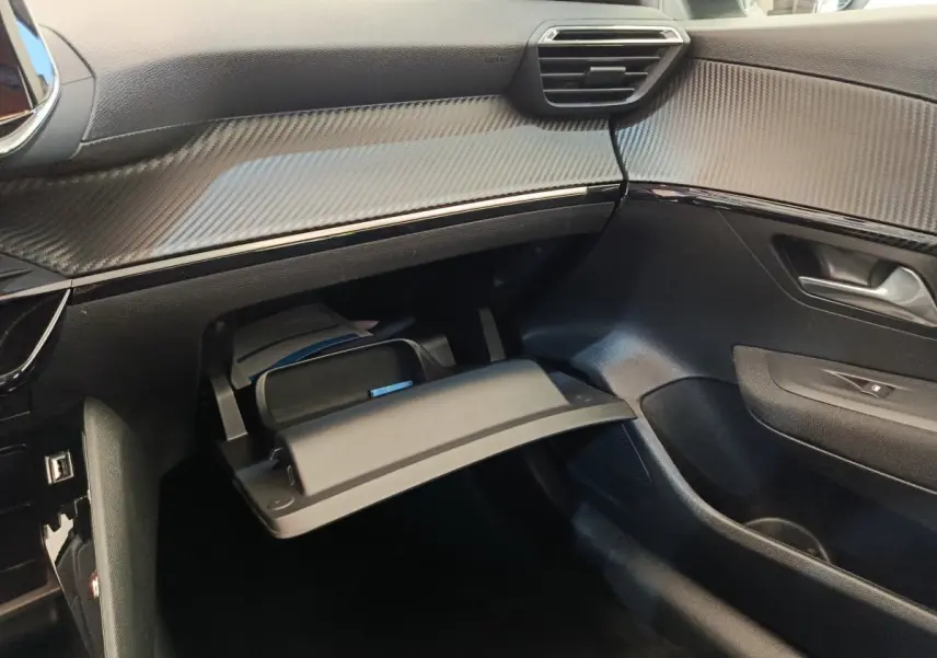 Vue intérieure côté passager du tableau de bord noir avec boîte à gants ouverte du Peugeot 208 électrique blanc 2021.