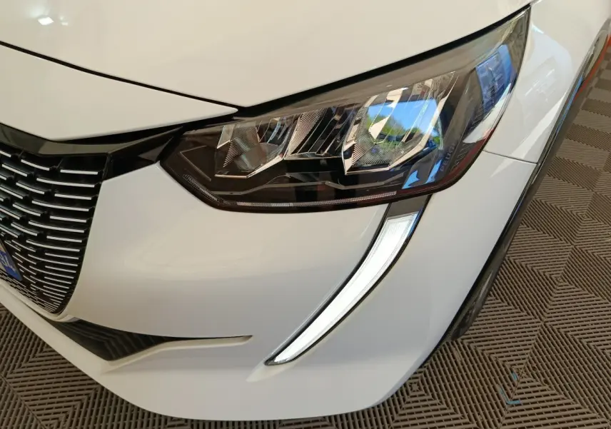 Gros plan sur le phare avant droit blanc d'une Peugeot 208 électrique avec signature lumineuse LED en forme de griffes.