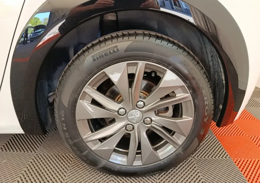Gros plan sur la roue avant droite de la Peugeot 208 électrique blanche, avec jante alliage et pneu Pirelli.