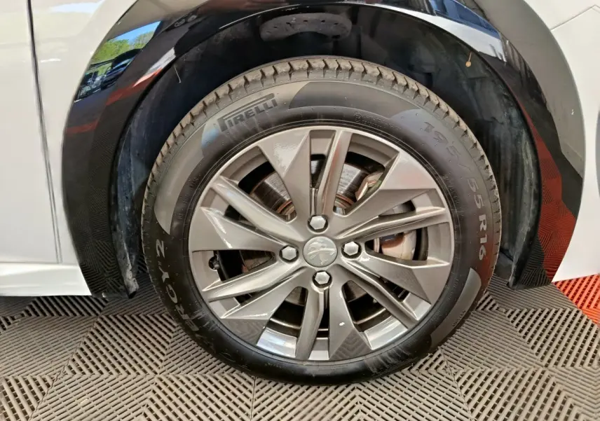 Gros plan sur la roue avant droite de la Peugeot 208 électrique blanche, jante alliage et pneu Pirelli.