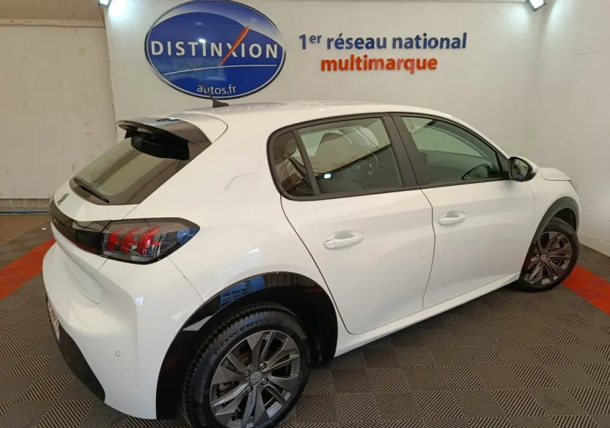 Peugeot 208 électrique blanc vue 3/4 arrière droit en intérieur avec jantes foncées et feux arrière LED distinctifs.