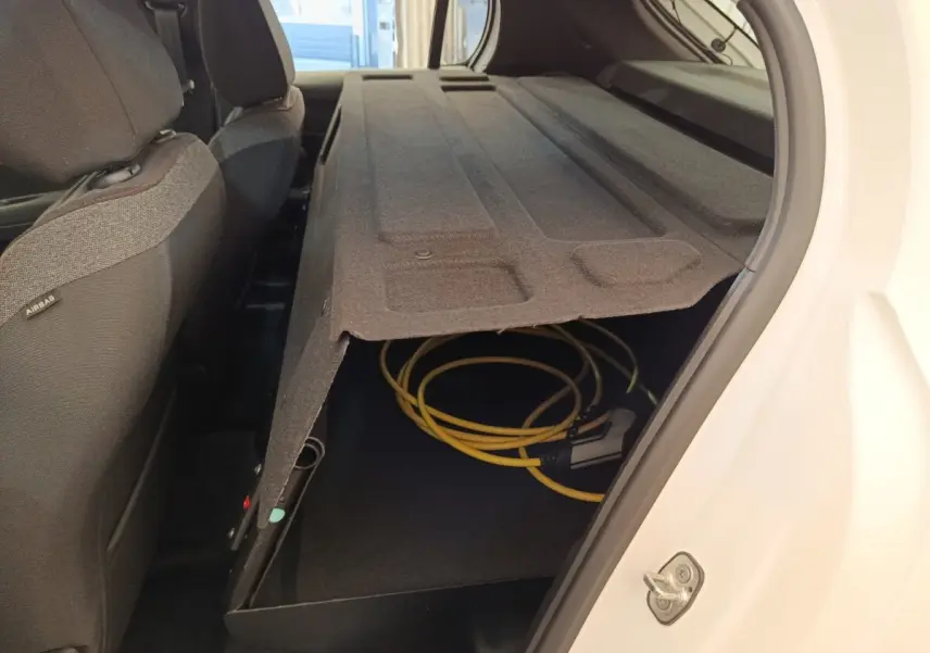 Vue intérieure arrière droite du coffre d'une Peugeot 208 électrique blanche avec câble de recharge rangé sous le plancher.