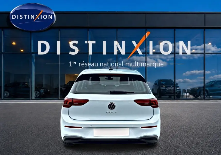 Vue arrière d'une Volkswagen Golf blanche garée devant une vitrine avec logo Distinxion.