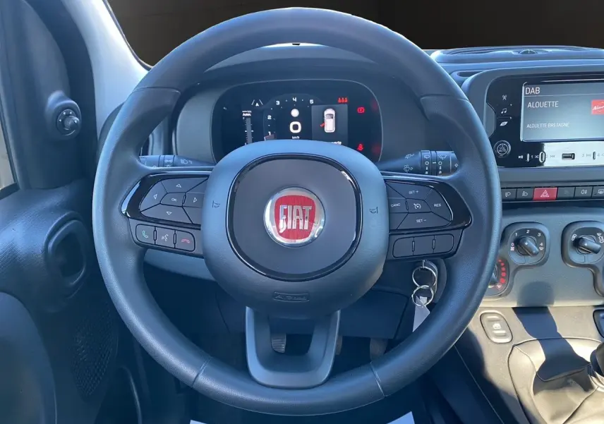 Vue rapprochée du volant noir FIAT Panda 2025 avec commandes intégrées et tableau de bord numérique allumé.