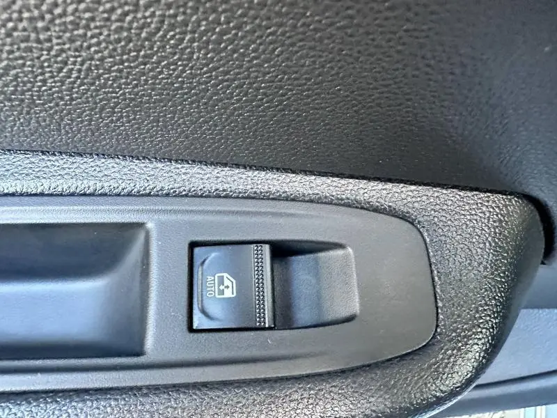 Gros plan sur l'interrupteur de lève-vitre automatique côté conducteur dans l'habitacle gris foncé de la Renault Clio 2025.