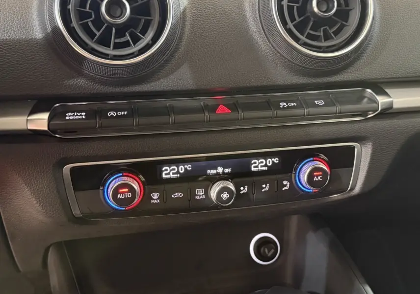 Détail de la console centrale de l'Audi A3 bleu, avec climatisation bi-zone réglée à 22°C et aérateurs ronds noirs.