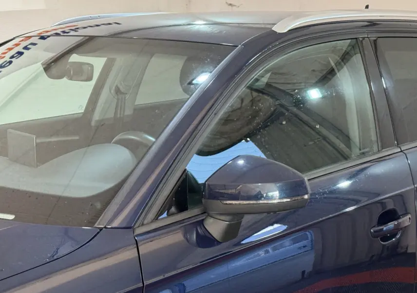 Vue latérale gauche rapprochée d'une Audi A3 bleu foncé avec rétroviseur et poignée de porte visibles.