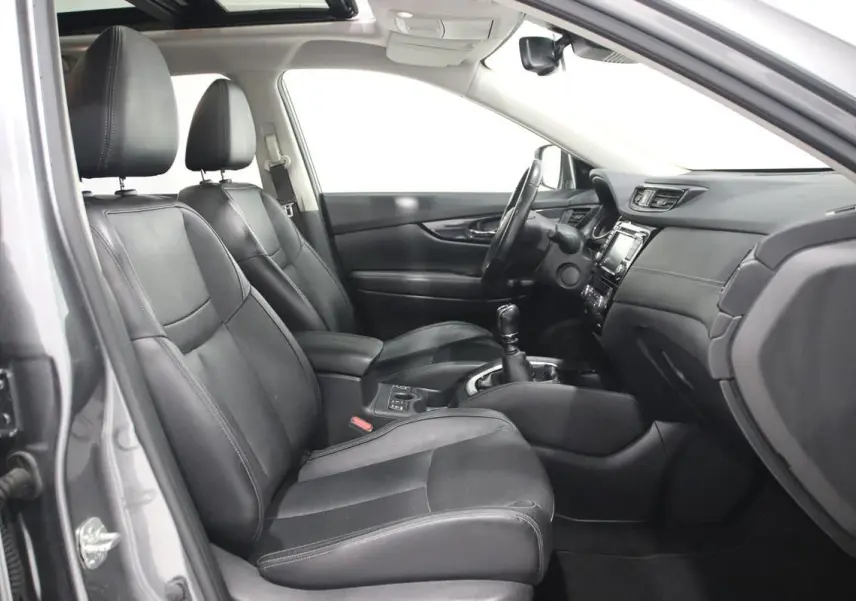 Vue intérieure côté conducteur du Nissan X-TRAIL gris métallisé 2021, sièges cuir noirs et boîte manuelle visible.