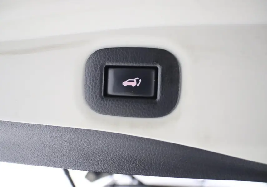 Bouton d'ouverture électrique du hayon sur le panneau intérieur d'un Nissan X-Trail gris métallisé.
