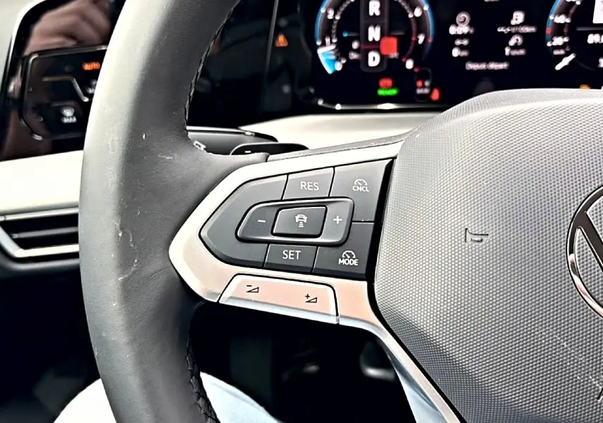 Gros plan sur le volant noir de la Volkswagen Golf 2026, avec commandes de régulateur de vitesse et tableau de bord numérique en arrière-plan.