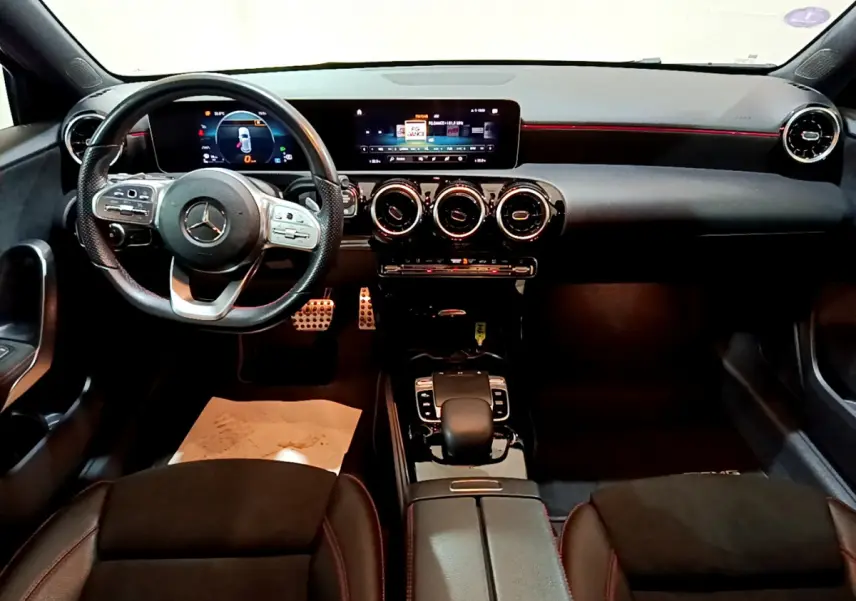Vue intérieure avant de la Mercedes Classe A 180 AMG Line 2019, tableau de bord noir avec éclairage rouge et volant cuir multifonction.