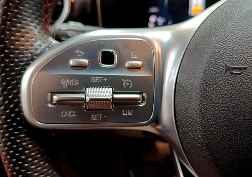 Gros plan sur les commandes du volant côté gauche en cuir perforé de la Mercedes Classe A 180 AMG Line noire.