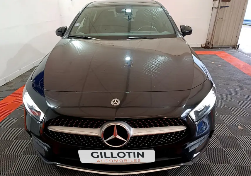 Vue avant d'une Mercedes Classe A 180 AMG Line noire avec calandre étoilée et phares LED allumés.