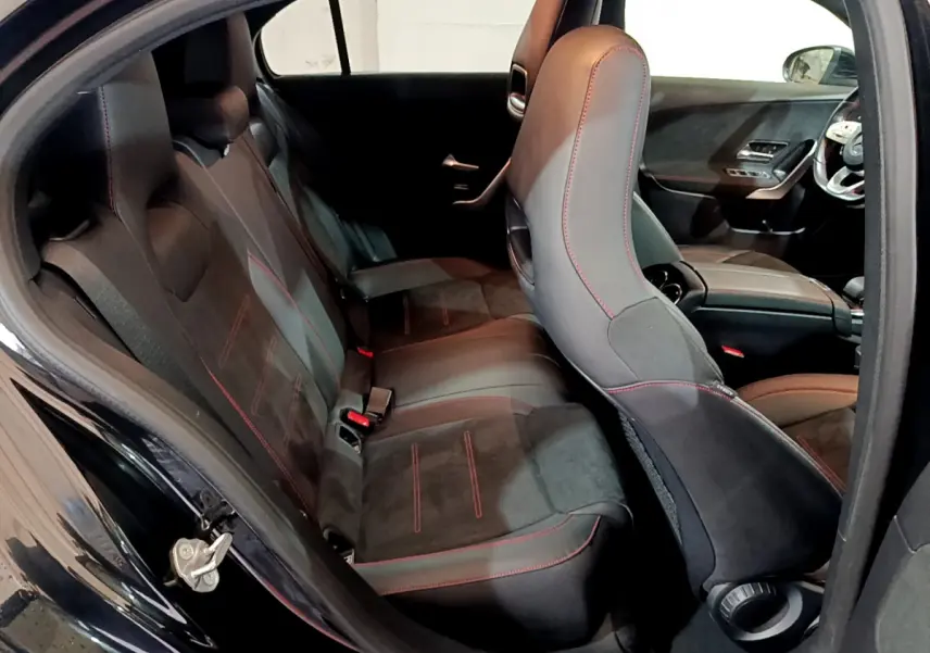 Vue intérieure côté gauche de la Mercedes Classe A 180 AMG Line noire, sièges sport noirs avec surpiqûres rouges.