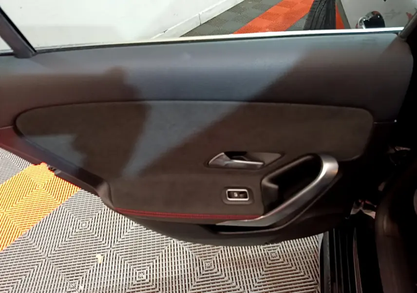 Gros plan sur la porte intérieure côté gauche noire avec surpiqûres rouges et poignée alu de la Mercedes Classe A 180 AMG Line.