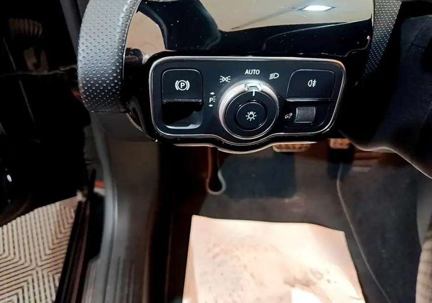 Gros plan sur la commande des phares et frein à main électrique dans l'habitacle noir d'une Mercedes Classe A 180 AMG Line.