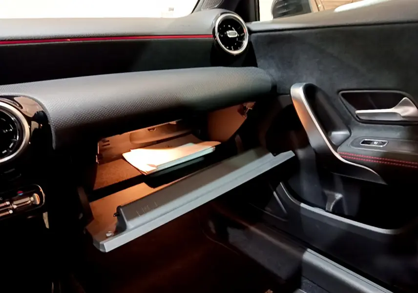 Intérieur de la Mercedes Classe A 180 AMG Line 2019, vue côté passager avec boîte à gants ouverte et détails en noir et rouge.