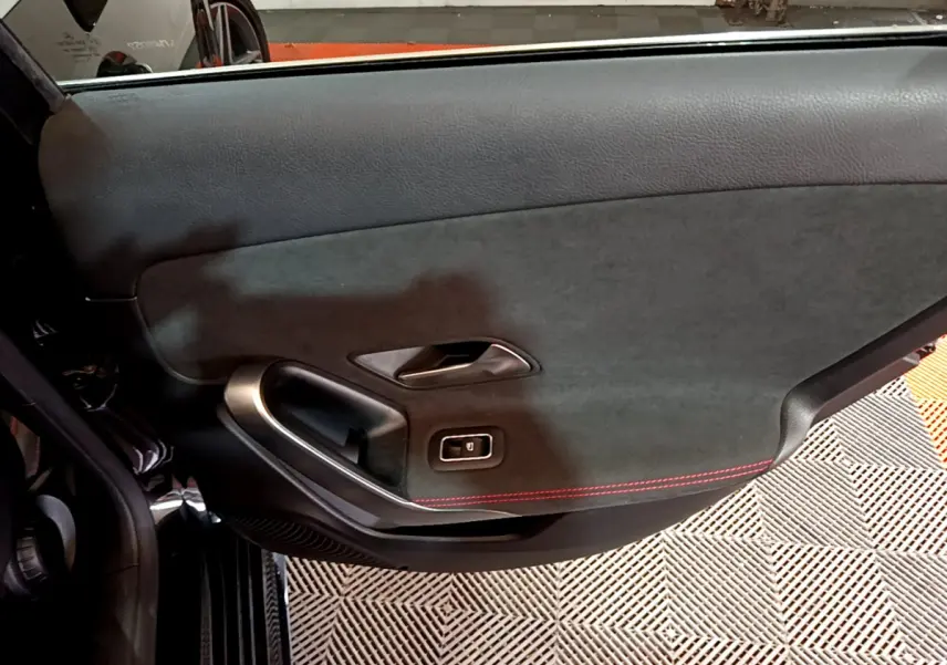 Gros plan sur la porte intérieure côté gauche d'une Mercedes Classe A 180 AMG Line noire avec surpiqûres rouges.