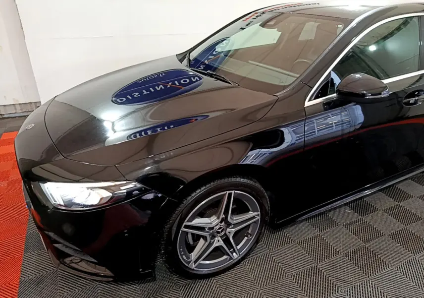Mercedes Classe A 180 AMG Line noire vue en 3/4 avant droit, avec jantes alliage et phares LED allumés.