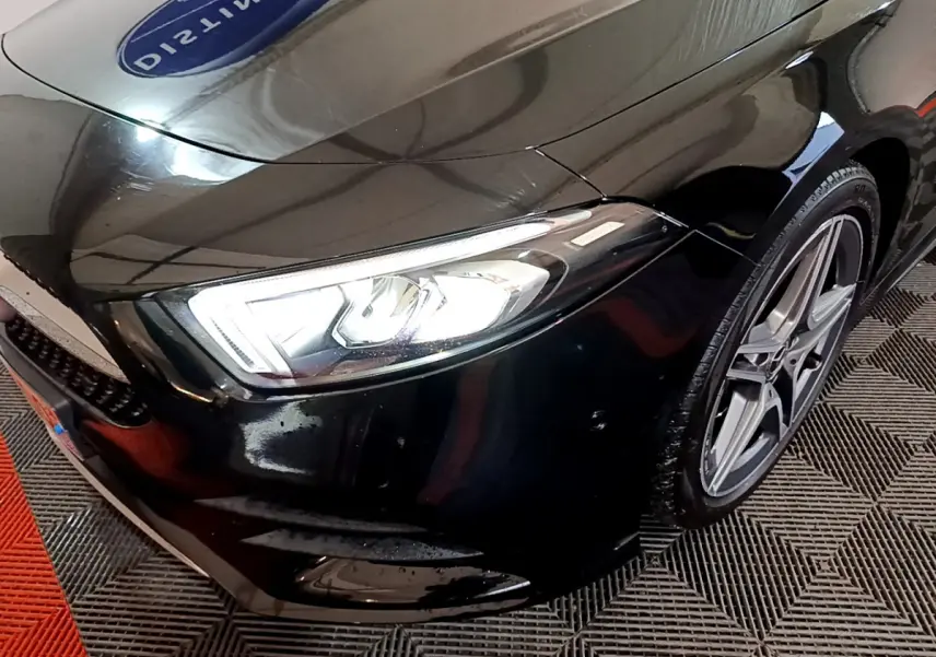 Gros plan sur l'avant droit noir brillant d'une Mercedes Classe A 180 AMG Line, mettant en valeur le phare LED et la jante alliage.