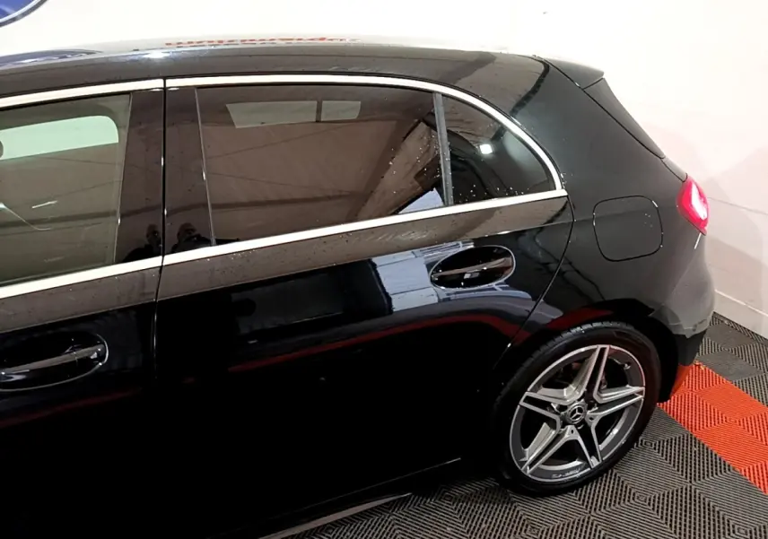 Vue latérale droite d'une Mercedes Classe A 180 AMG Line noire, mettant en valeur la jante alliage et la ligne de toit chromée.