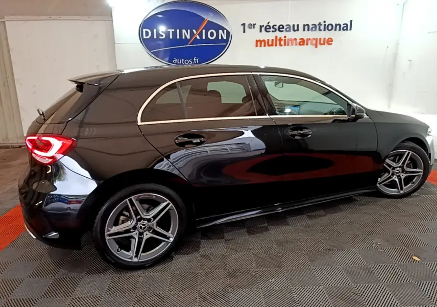 Vue de profil côté droit d'une Mercedes Classe A 180 AMG Line noire avec jantes alliage et feux arrière LED allumés.