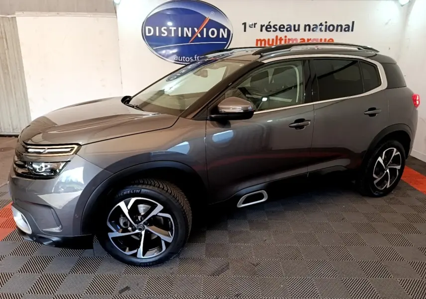 Vue de profil droit du Citroën C5 Aircross gris foncé avec jantes alliage et barres de toit chromées en intérieur showroom.