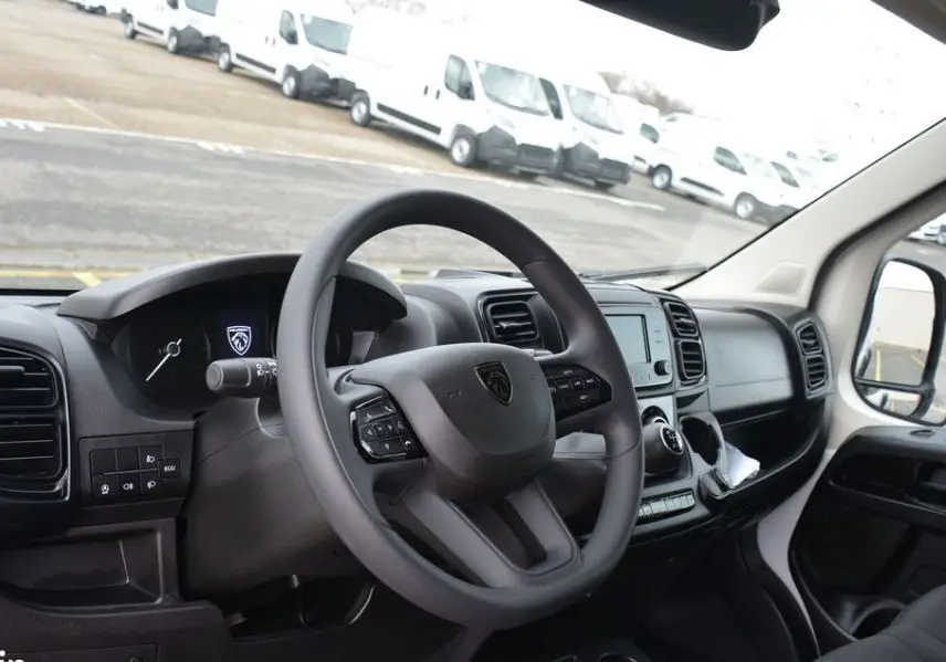 Vue intérieure côté conducteur du Peugeot Boxer Fourgon blanc Icy, volant cuir avec commandes intégrées et tableau de bord moderne.
