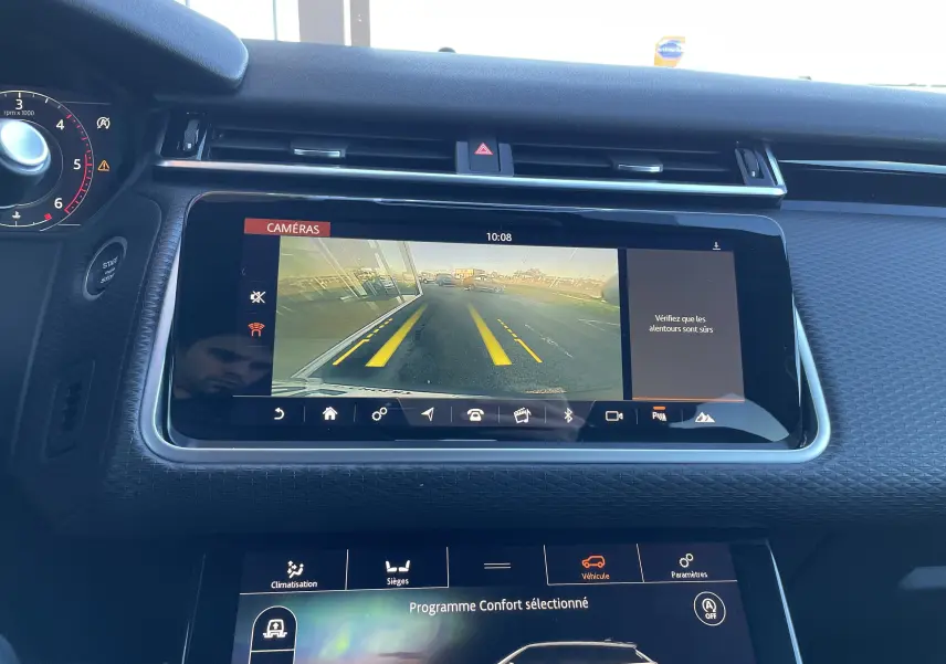 Vue rapprochée de l'écran central du Range Rover Velar gris, affichant la caméra de recul avec lignes de guidage jaunes.