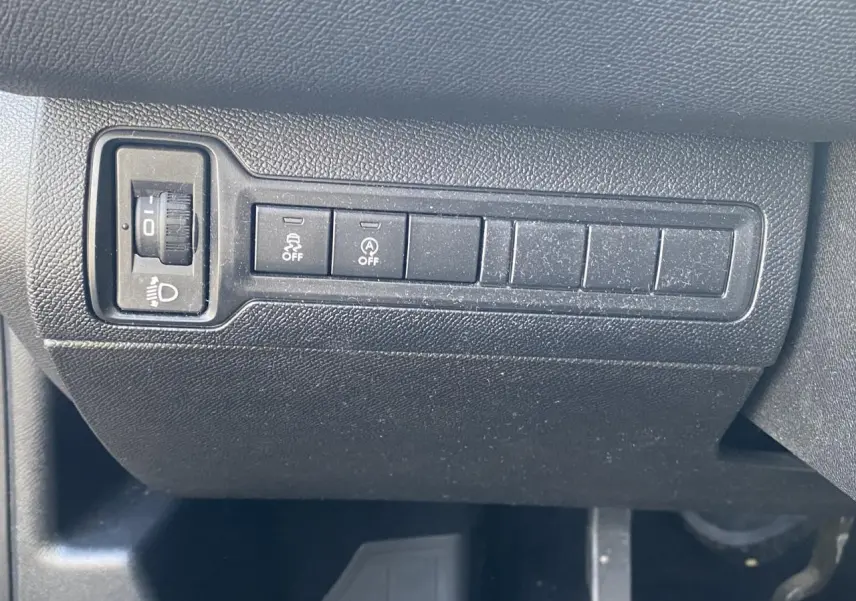 Gros plan sur les commandes de réglage des phares et des aides à la conduite sur la planche de bord noire d'une Peugeot 308 bleu foncé.