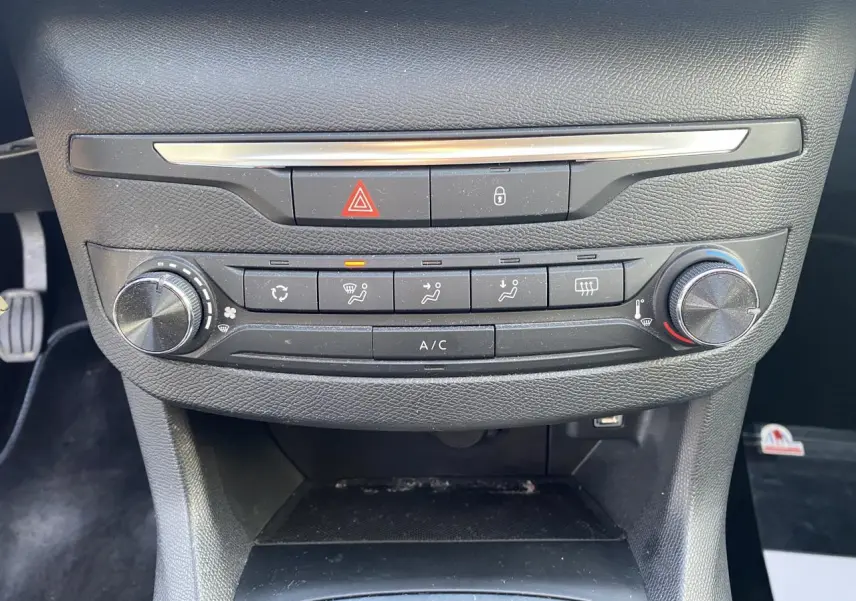 Vue rapprochée de la console centrale de la Peugeot 308 bleu foncé, montrant les commandes de climatisation et les boutons d'alerte.