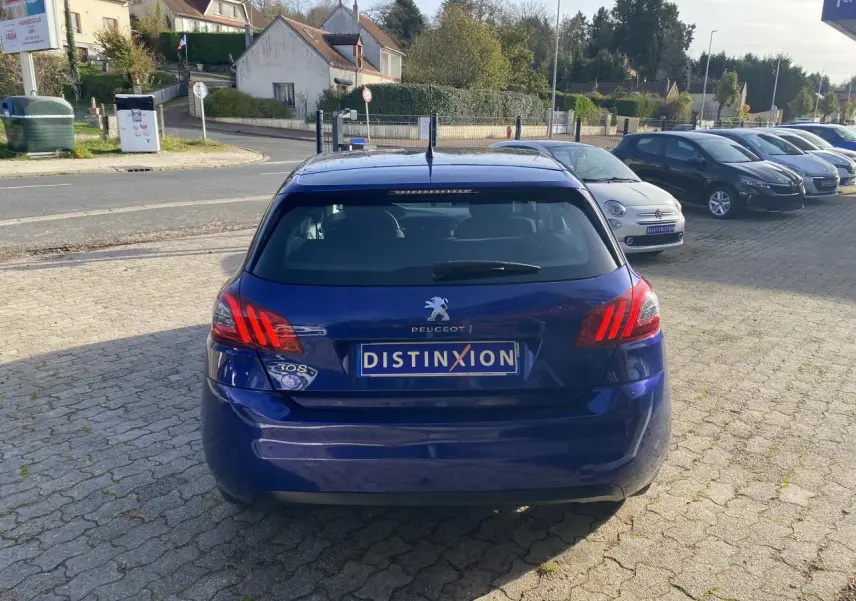 Vue arrière d'une Peugeot 308 bleu foncé avec feux arrière allumés et plaque d'immatriculation Distinxion.