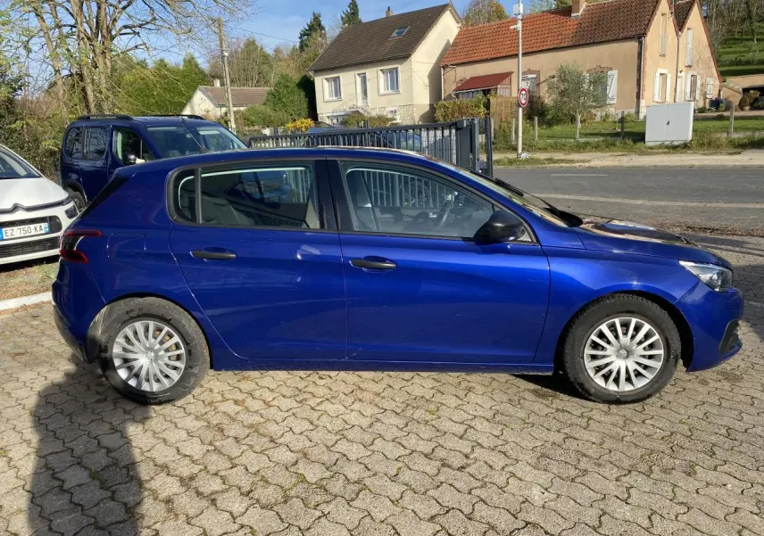 Peugeot 308 bleu foncé vue de profil côté gauche, stationnée sur un sol pavé avec roues en alliage.