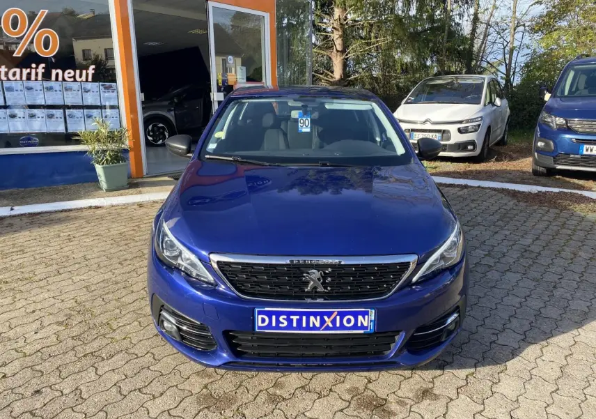 Peugeot 308 bleu foncé vue de face, avec calandre chromée et projecteurs antibrouillard halogènes visibles.