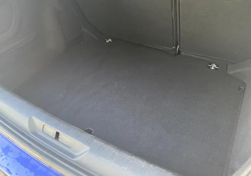 Coffre ouvert d'une Peugeot 308 bleu foncé, montrant le tapis de coffre propre et le dossier de banquette arrière rabattable.