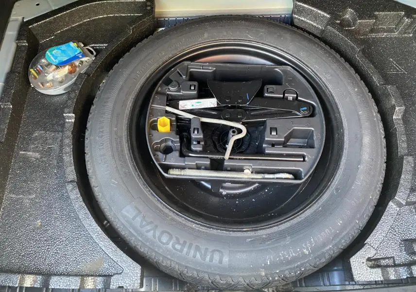 Vue plongeante sur la roue de secours et les outils de bord du coffre d'une Peugeot 308 bleu foncé de 2017.