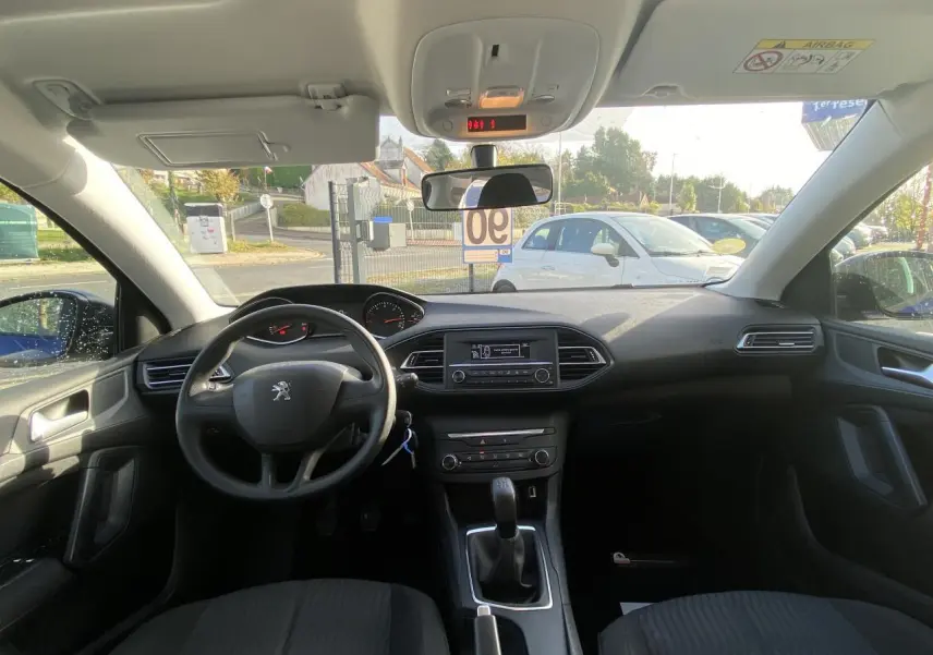 Vue intérieure avant de la Peugeot 308 2017, tableau de bord et volant noir avec boîte manuelle visible.
