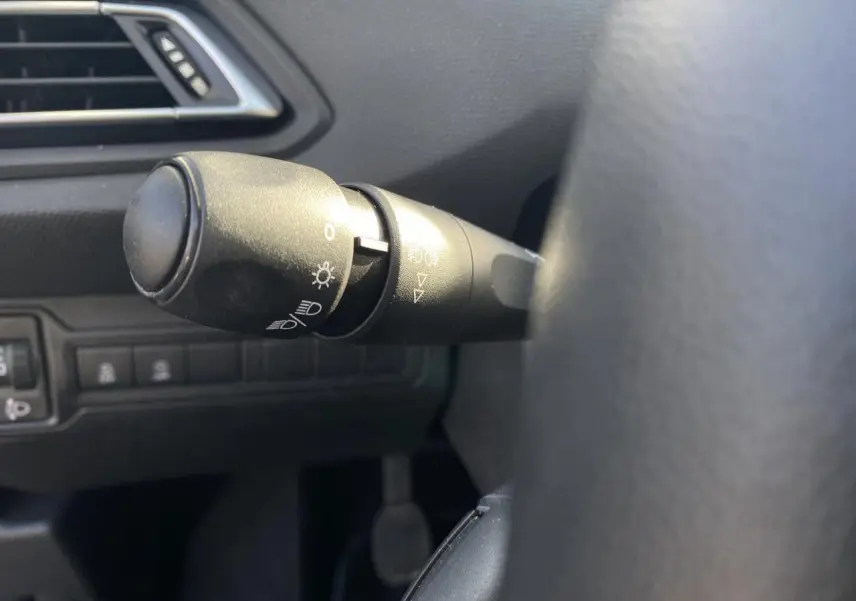 Gros plan sur la commande des phares à gauche du volant dans l'habitacle sombre d'une Peugeot 308 bleu foncé de 2017.