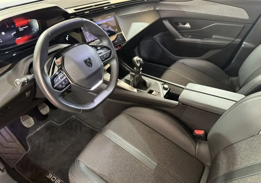 Intérieur noir de la Peugeot 308 2023, vue côté conducteur, volant cuir, écran tactile et boîte manuelle visibles.